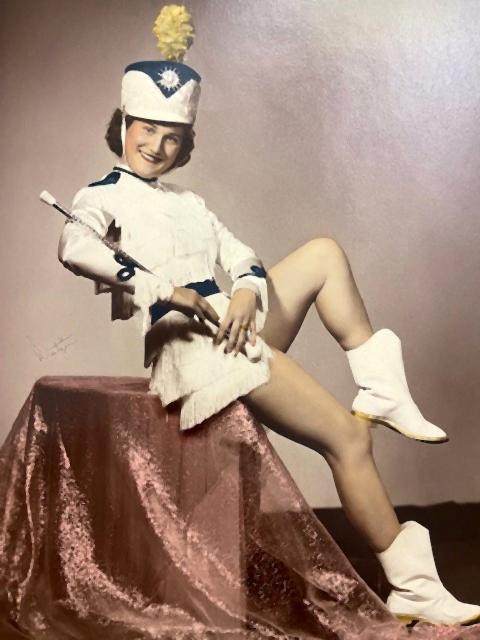 A woman named Kathleen, wearing a dance or band uniform, is sitting for a photo.