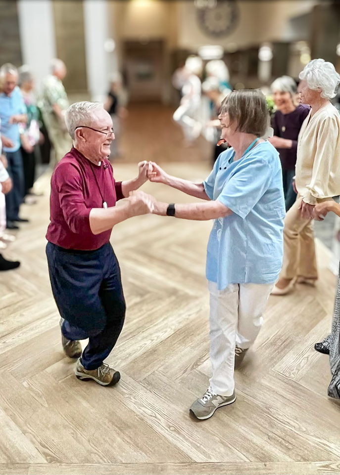 A senior couple dance together, surrounded by other cheerful residents at a dance event.