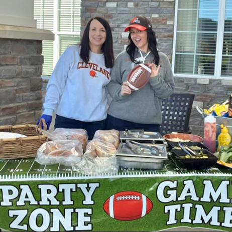 Two team members smile beside a football themed party table filled with themed food.