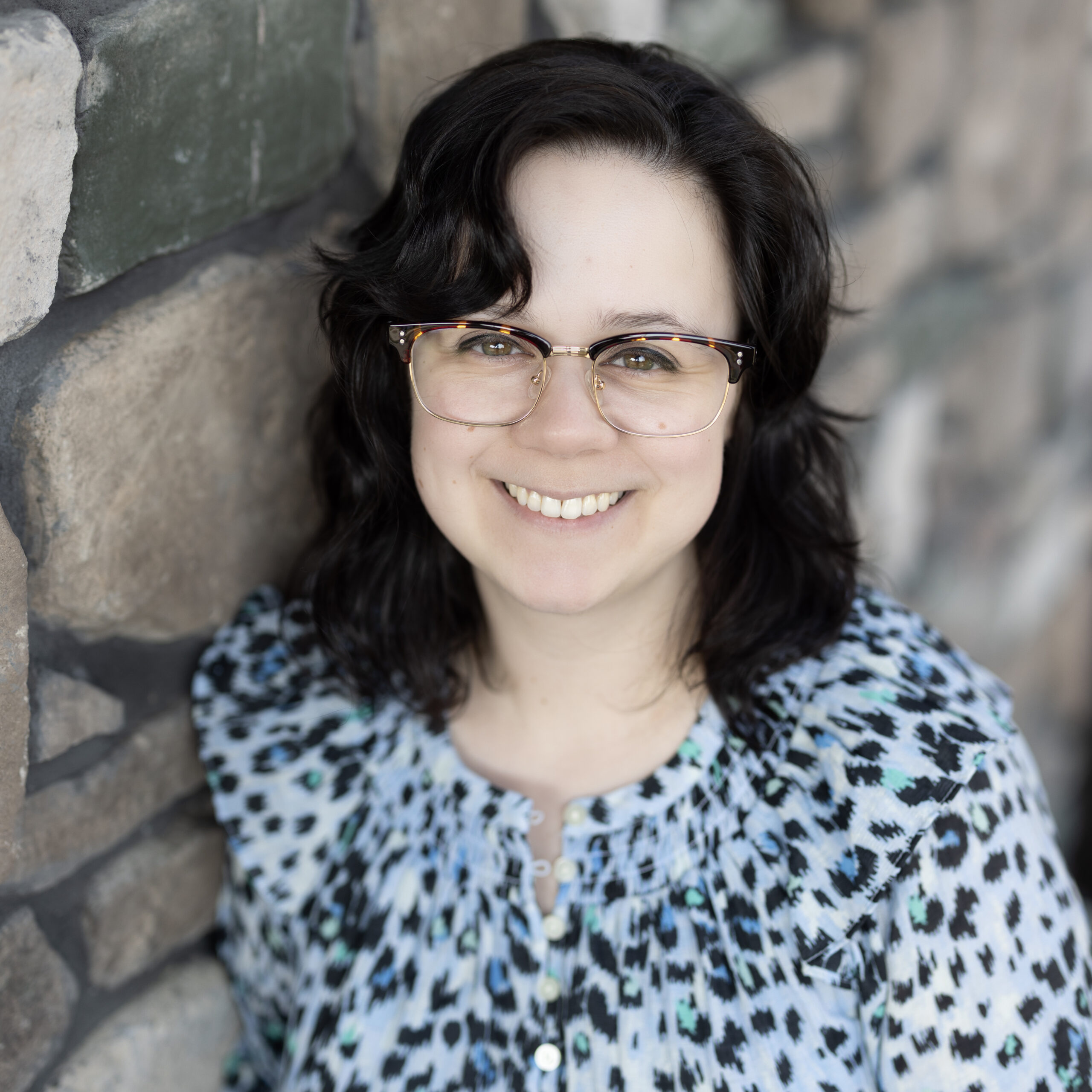 Bethany Sara, Business Office Director at Vitalia Strongsville, smiling while leaning against a stone wall in a patterned blouse.