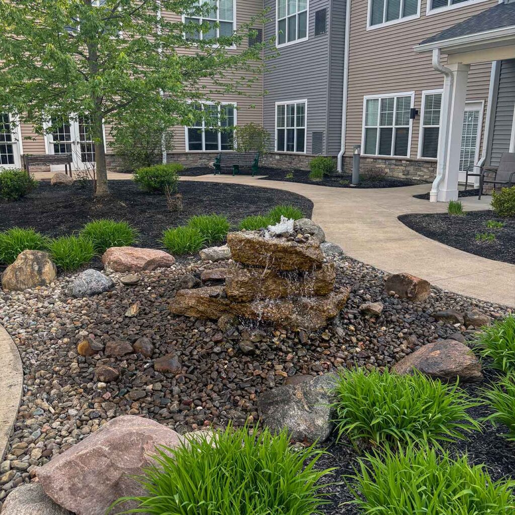 A beautifully landscaped outdoor area, featuring walkways, mulch beds, large stones, and ornamental grasses.