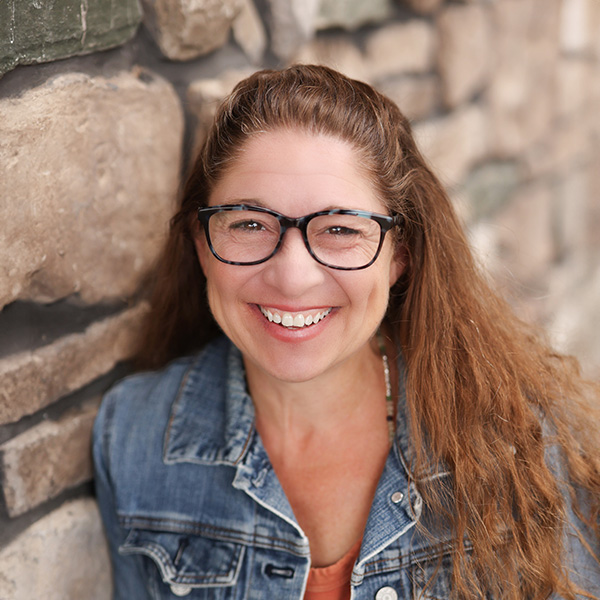 Crystal Lamb, Senior Living Director at Vitalia North Royalton, smiling in a denim jacket while standing against a stone wall.